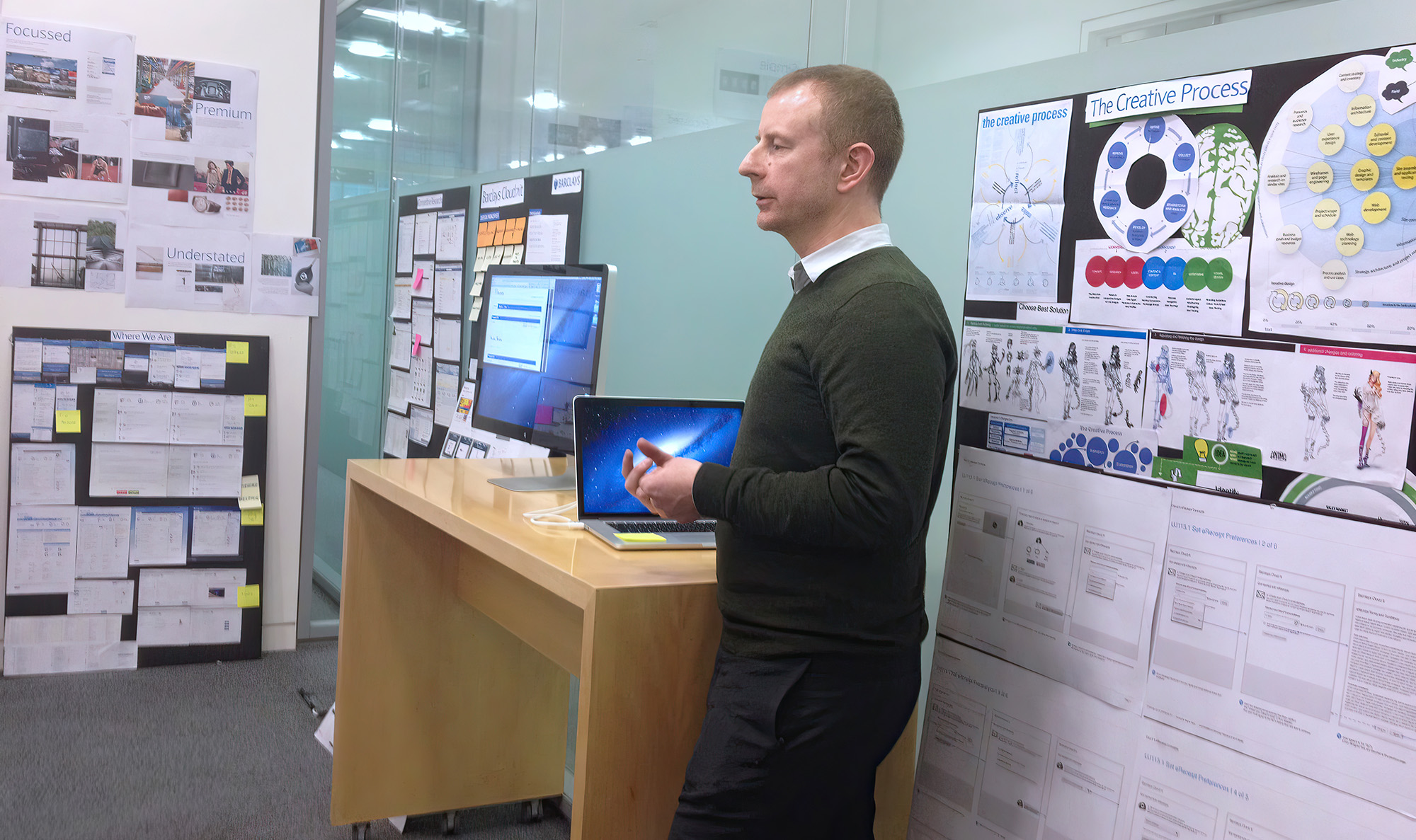 Steven Wise presenting a show and tell to stakeholders surrounded by UX artefacts stuck on the walls