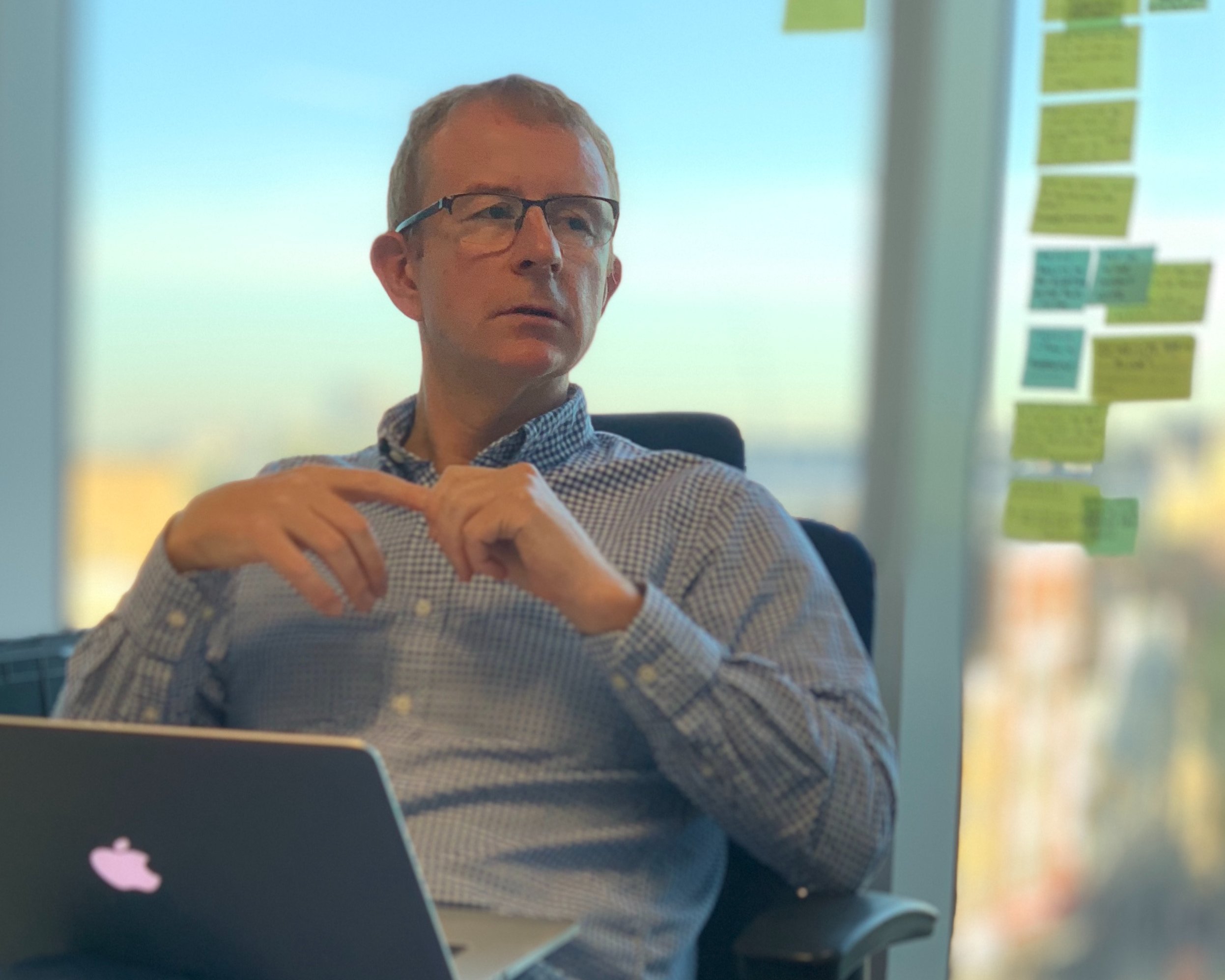 Steven Wise sitting in a chair with an Apple laptop and PostIt notes stuck on the window behind him